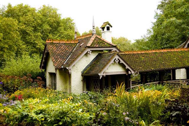 A white cottage with a tiled roof and garden full of colourful flowers is seen near the Pelican Pool in the park.