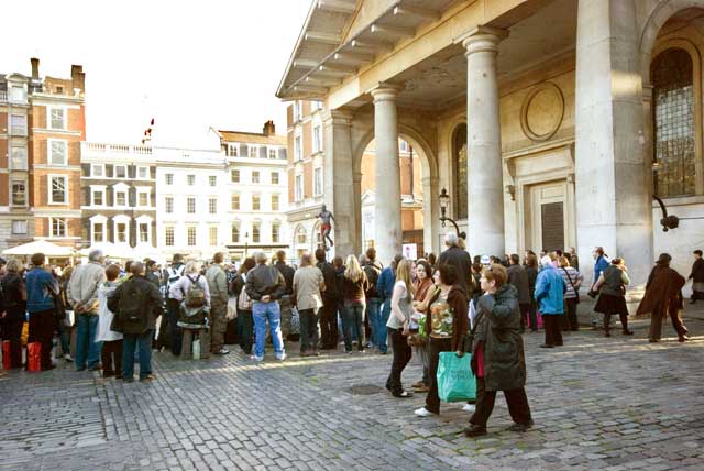 Entertainment is being enjoyed by a large crowd at the piazza at Covent Garden, near the London Transport Museum.