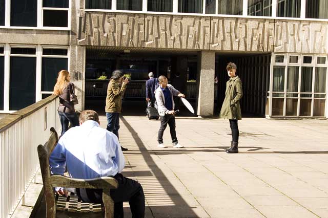 A male teenage model poses to be photographer on one of the bridges of the high level walkways of the Barbican Centre.