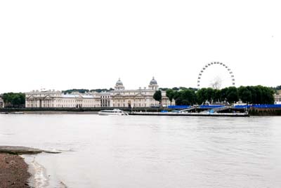 The white stone buildings of the Royal Naval Hospital can be seen across the river from the Isle of Dogs. In the background is a Ferris wheel. 