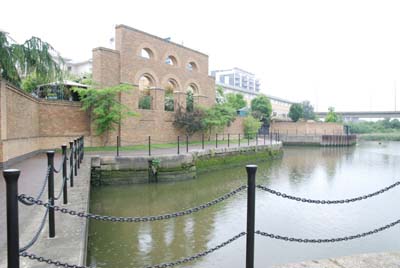 East India Dock has now been turned into a nature reserve. In the foreground is the water of the dock and in the background a high brick wall with the arches, one of the buildings left from the time that this was a very busy place.