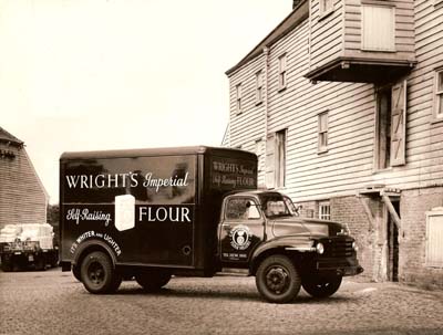 A vintage van stands in front of the old  mill in this historic sepia picture of Wrights Flour Mill; the mill is still producing flour today.